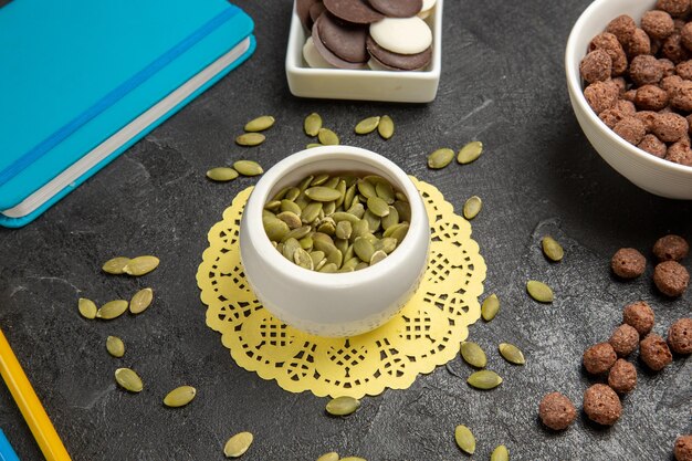 Half-top view fresh pumpkin seeds with cookies on dark-grey background rainbow color seed candy