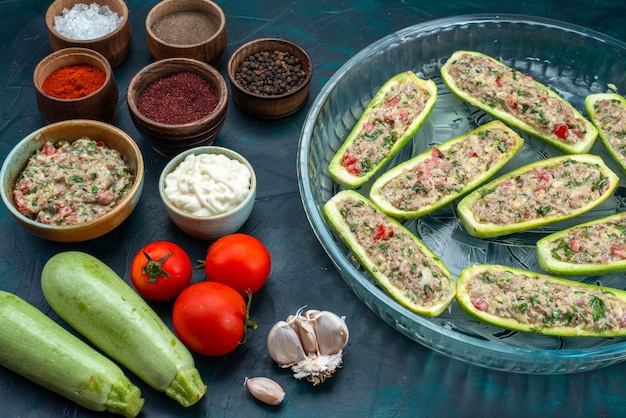 Free photo half-top view raw squashes with spicy minced meat along with vegetables on dark blue desk.