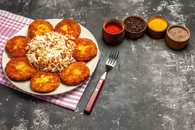 Half-top view tasty fried cutlets with rice and seasonings on a dark surface meat rissole meal