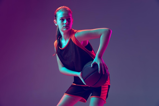 Halflength portrait of young girl basketball athlete training playing isolated over purple background in neon