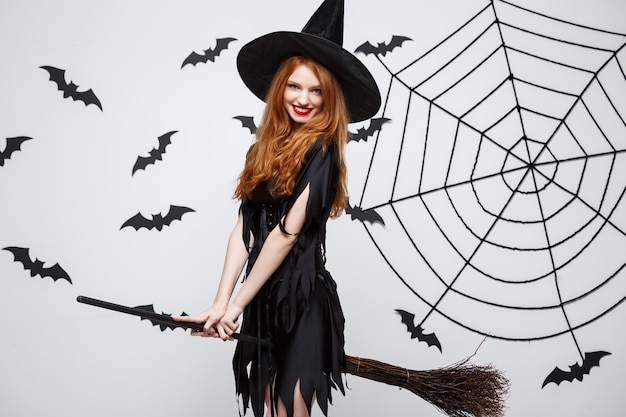 Free Photo halloween concept  happy elegant witch enjoy playing with broomstick halloween party over grey wall