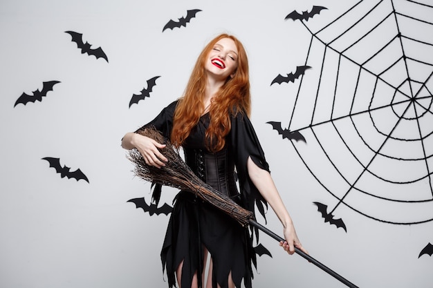 Free Photo halloween concept  happy elegant witch enjoy playing with broomstick halloween party over grey wall