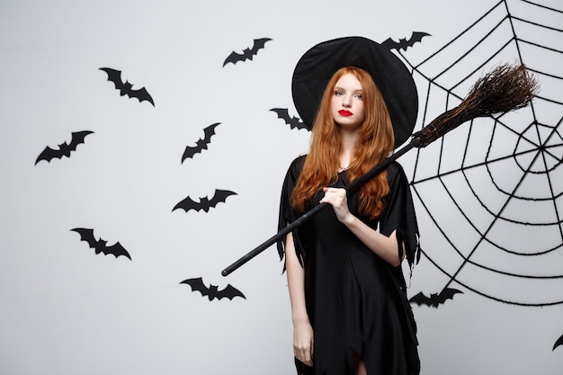 Free Photo halloween concept  happy elegant witch enjoy playing with broomstick halloween party over grey wall