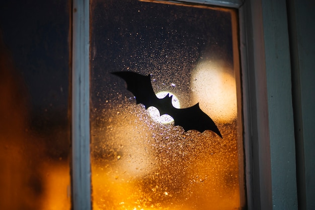 Halloween paper bat decorating window covered with raindrops