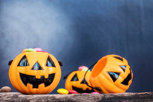 Free photo halloween pumpkin face buckets with colorful candy inside on old wooden plank