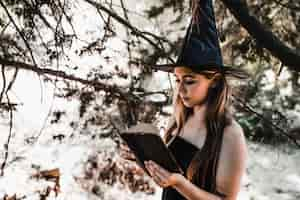 Free photo halloween witch holding old tome in sunny forest