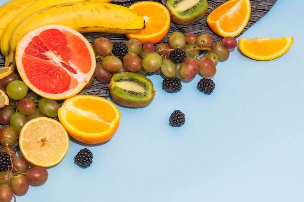 Free photo halved citrus fruits; grapes; banana; kiwi on blue background