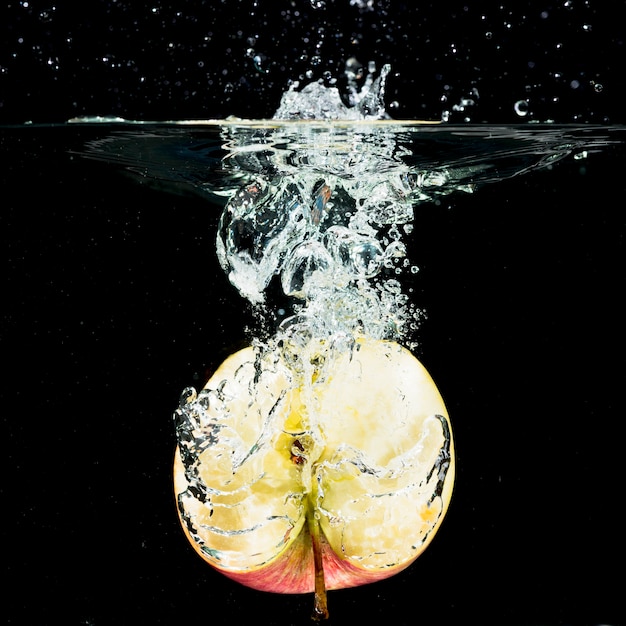 Free Photo halved fresh apple falling into clean water against black background