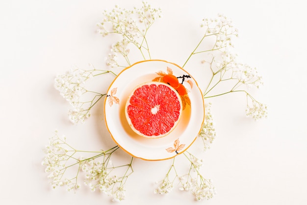 Free photo halved grapefruit on ceramic plate decorated with baby's-breath flowers on white background