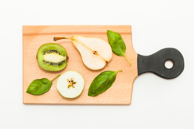 Free photo halved kiwi; pears; apple and basil on chopping board against white background