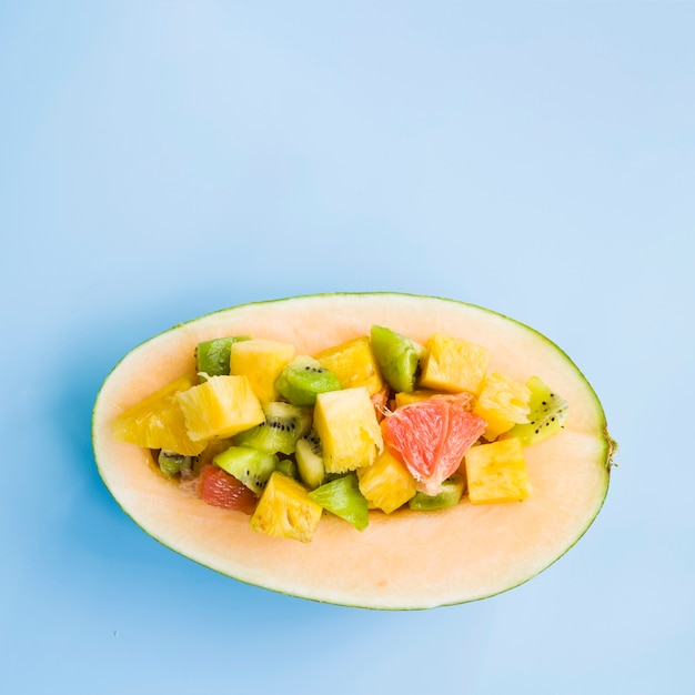 Halved melon with slices of fruits on blue background