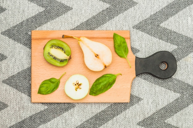 Free photo halved pear; apple slice and basil leaves on wooden chopping board