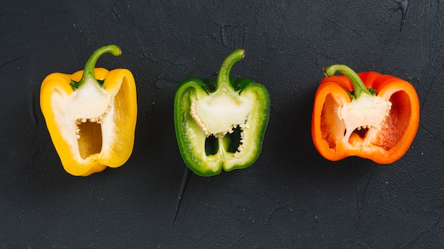 Free photo halved yellow; green and red bell pepper on black concrete textured background