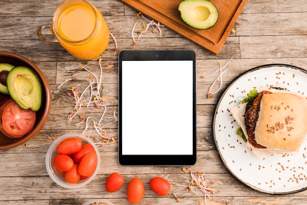 Free photo hamburger; juice jar; tomatoes; avocado and sprout and digital tablet on wooden table