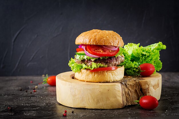 Hamburger with beef meat burger and fresh vegetables on dark table. Tasty food.