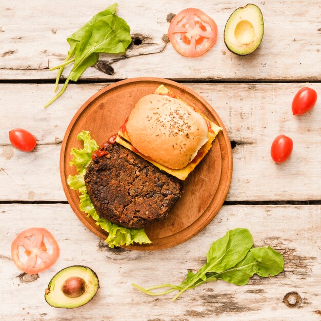 Hamburger with lettuce and cheese on circular wooden board on table