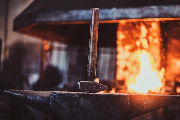 Hammer on anvil at dark blacksmith workshop with fire in stove at background.