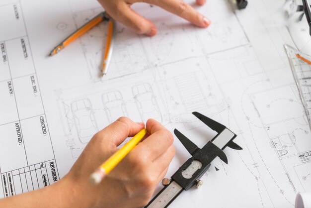 Hand over Construction plans with yellow helmet and drawing tool