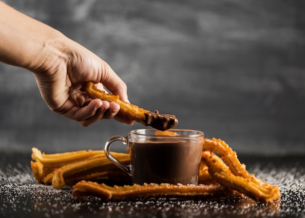 Hand dipping a fried churros in chocolate front view