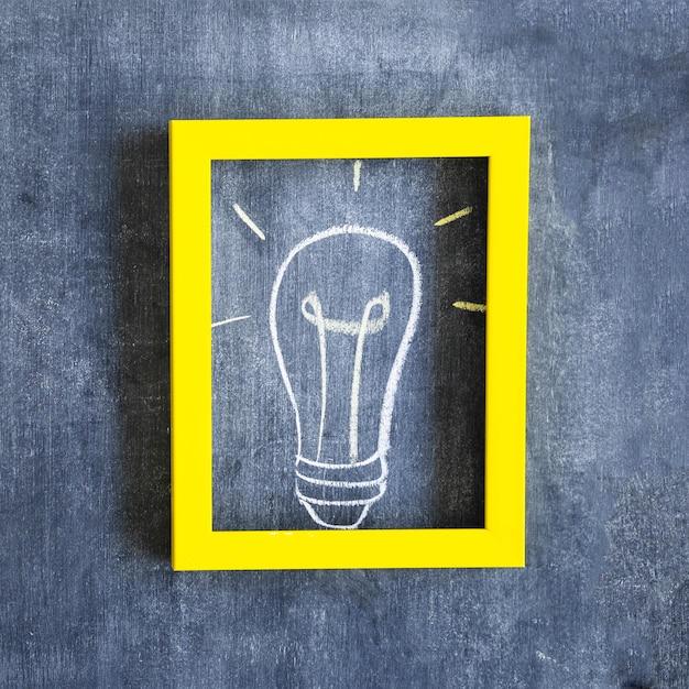 Free photo hand drawn light bulb inside the frame with yellow border on chalkboard