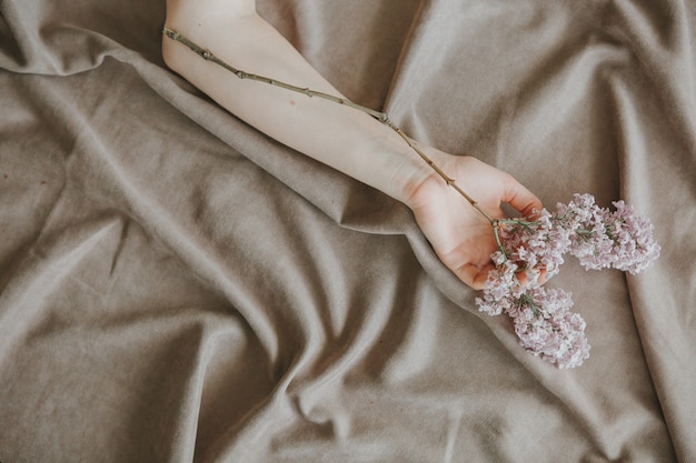 hand of a girl with a lilac branch on a bed on a crumpled sheet