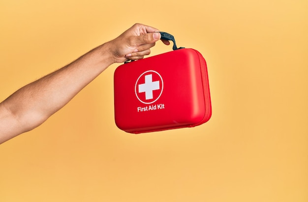 Free photo hand of hispanic man holding first aid kit over isolated yellow background.