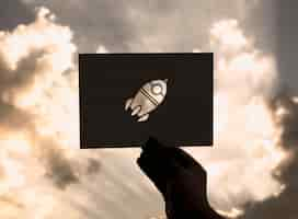 Free photo hand hold space rocket paper carving with sky background