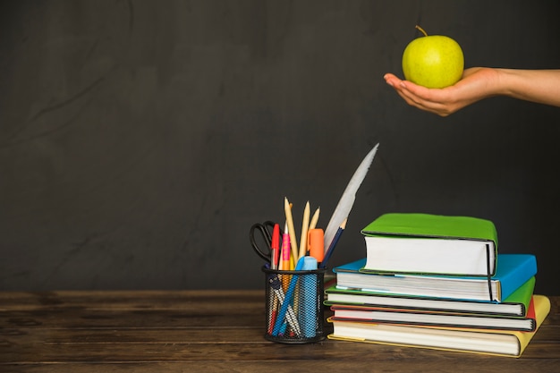 Hand holding apple on workplace with books and stationery 