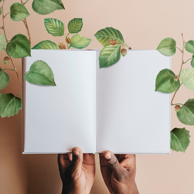 Free Photo hand holding blank notebook page with green leaves