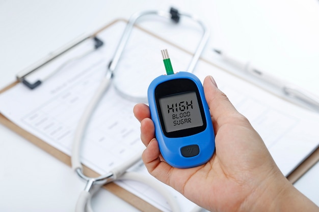 Free photo hand holding a blood glucose meter measuring blood sugar, the background is a stethoscope and chart file