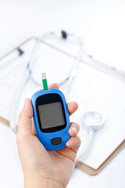 Free photo hand holding a blood glucose meter measuring blood sugar, the background is a stethoscope and chart file