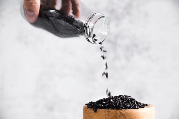 Free photo hand holding bottle with black rice near bowl