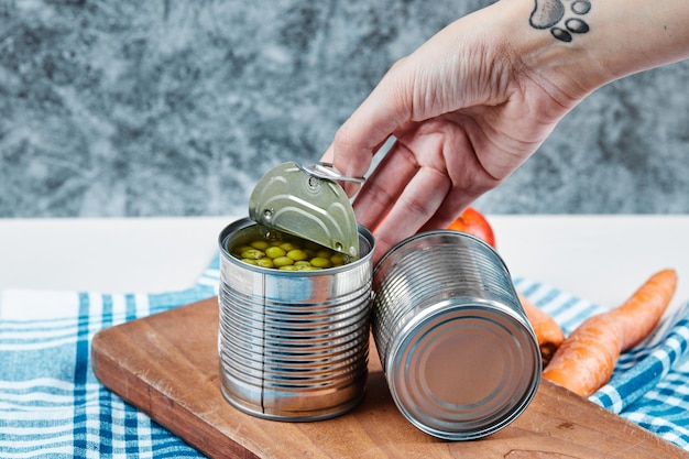 Free photo hand holding a can of boiled green peas on a white table with vegetables and tablecloth.