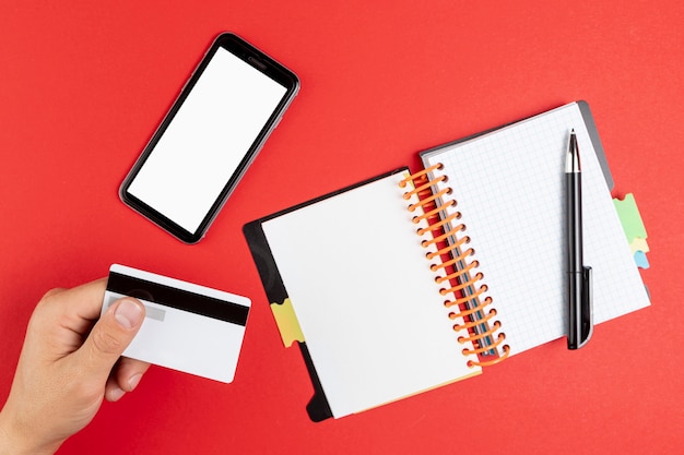 Hand holding a card next to a notebook and phone mock up