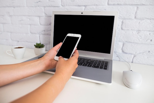 Hand holding cellphone over the open laptop on the desk