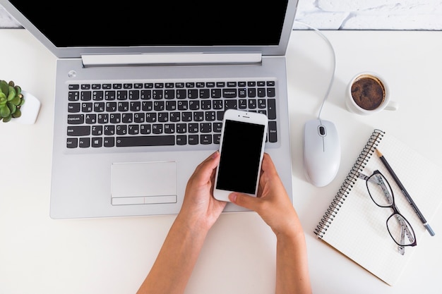 Hand holding cellphone over the open laptop on the desk