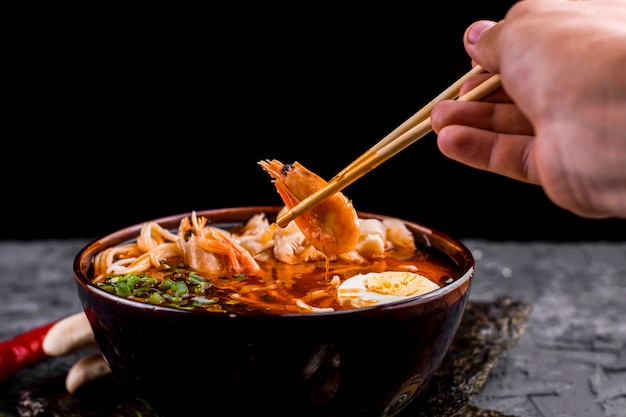 Free photo hand holding chopsticks with shrimp ramen