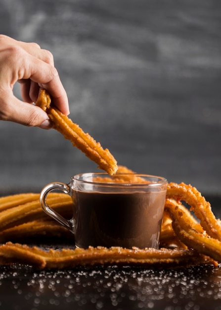 Hand holding a churros above a glass of chocolate