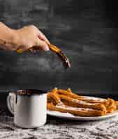 Free photo hand holding a churros with chocolate and a cup