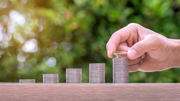 Hand holding coin and stack of money on wood table Pension fund concept