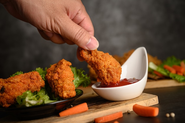 Hand holding crispy fried chicken dipped in tomato sauce