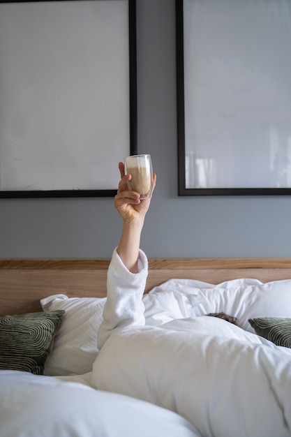 Hand holding a cup of coffee at home in bed