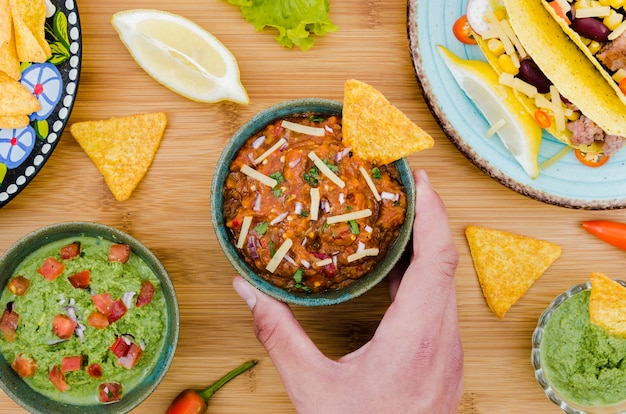 Free Photo hand holding cup of garnish with nacho near mexican food