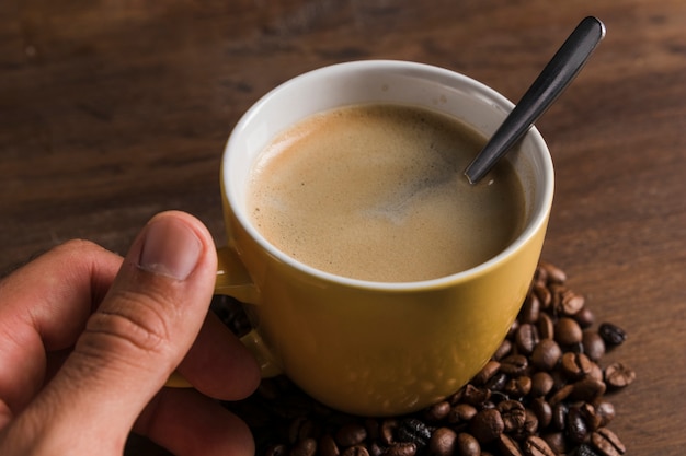 Hand holding cup with spoon and coffee