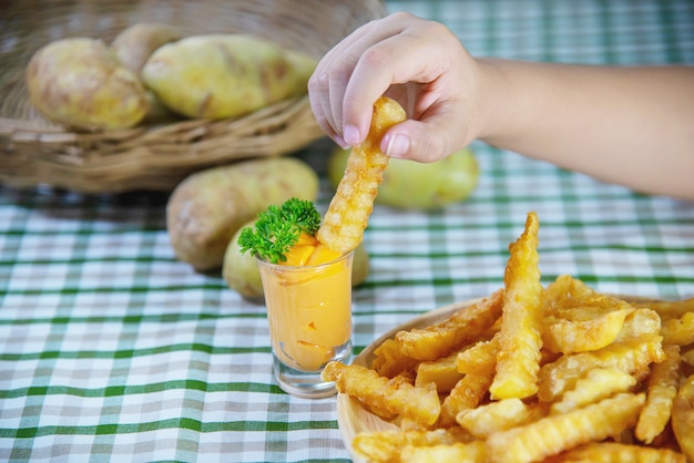 Hand holding delicious fried potato on wooden plate with dipped sauce 