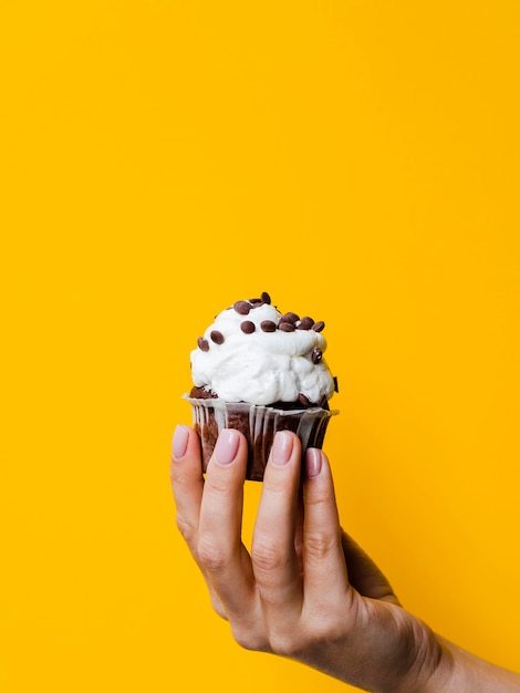 Free photo hand holding delicious muffin on yellow background