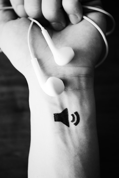 Free photo hand holding earphones with tattoo