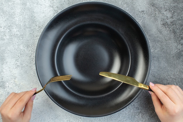 Hand holding elegant fork and knife on black dinnerware set on isolated gray ice surface with free space