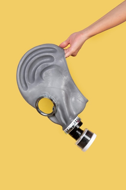 Free photo hand holding gas mask on yellow background