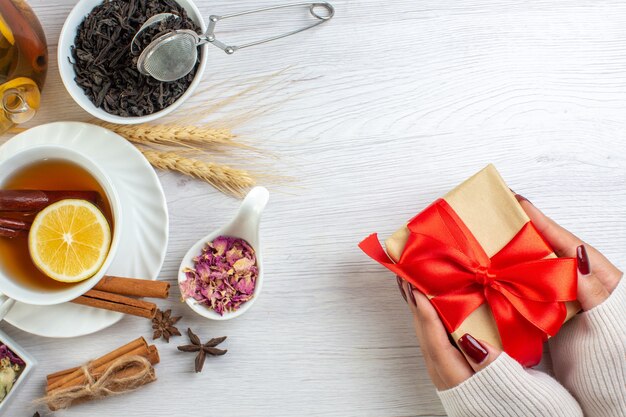 Hand holding gifts with red ribbon and tea break with cinnamon